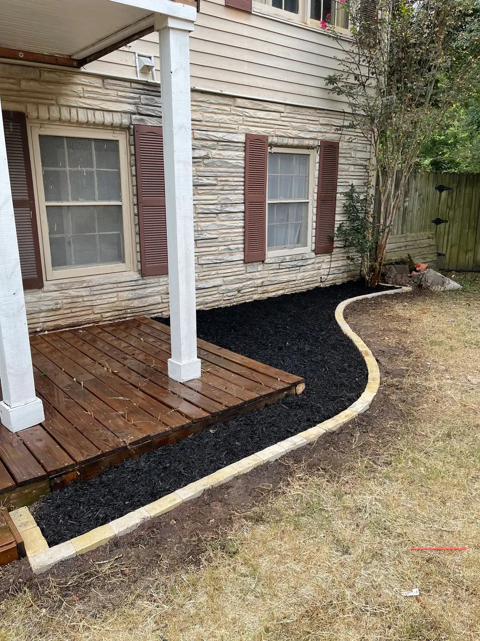 Curved mulch bed with edging along a porch and deck