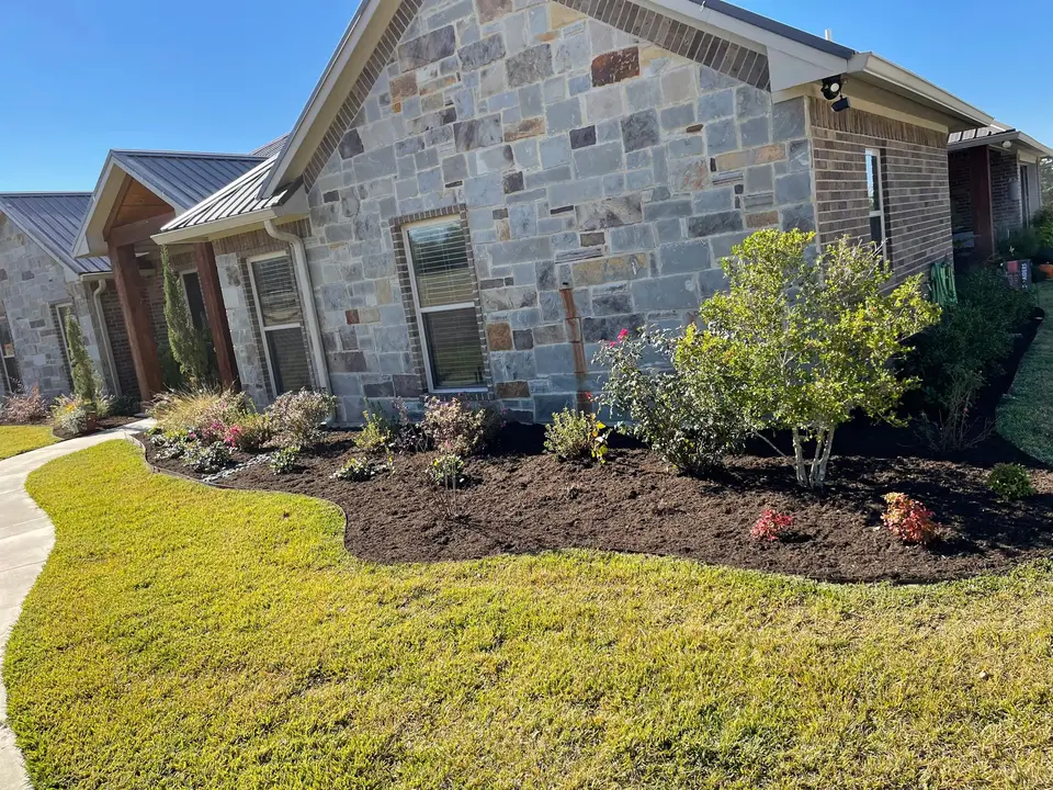 Fresh mulch bed with new plantings and a trimmed lawn in front of a stone house